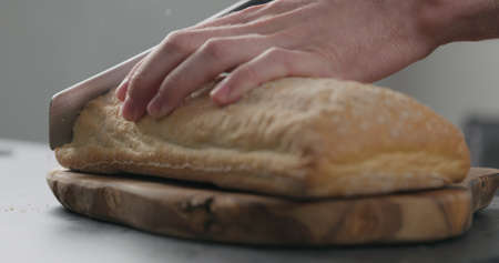 closeup of slicing freshly bakled ciabatta bread on olive board