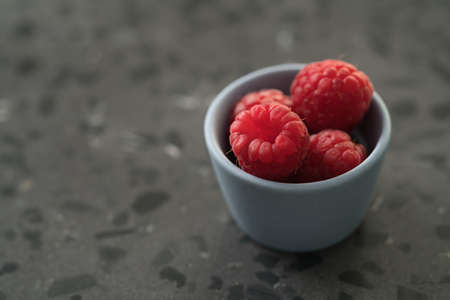 Fresh ripe raspberries in small blue bowl on concrete backgroundの写真素材