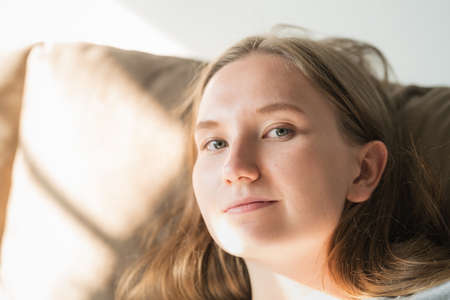 young woman relaxing on a couch with sunlight from a windowの写真素材