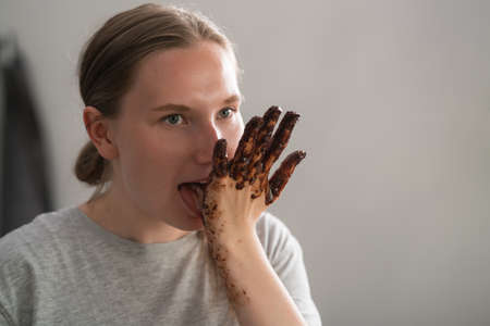 cheerful girl licking chocolate from her hands after making candies