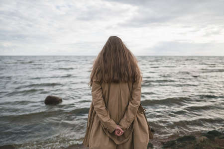 pretty girl walking on a beach in beige trench coat from behindの写真素材