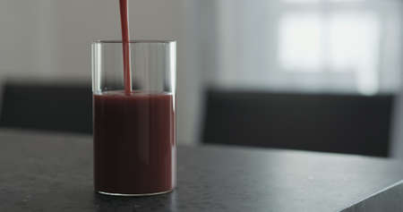 pour berry smoothie in highball glass on concrete countertop