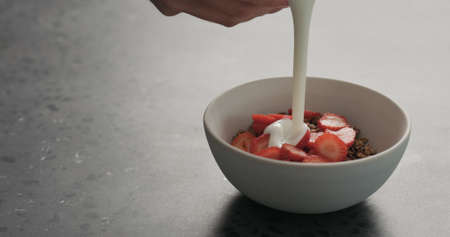 man hand pour chocolate granola with strawberries with white yogurt on a concrete countertopの写真素材
