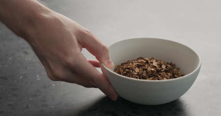 man hand place white bowl with chocolate granola on a concrete countertopの写真素材