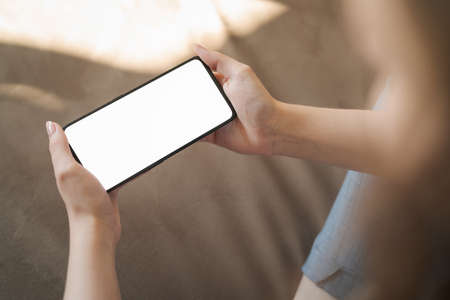 Young woman hold smartphone with white screen while sitting on a couch