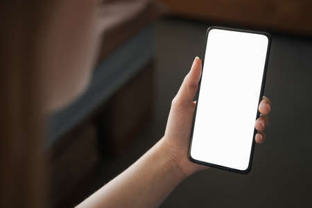 Young woman hold smartphone with white screen while sitting on a couch