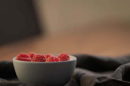 Yogurt with fresh raspberries in blue ceramic bowl on walnut table with copy space