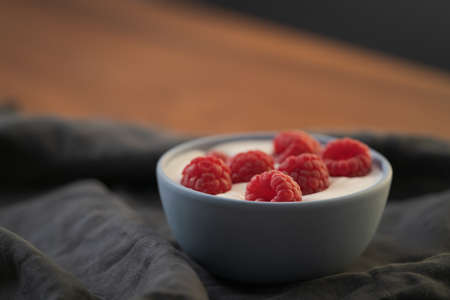 Yogurt with fresh raspberries in blue ceramic bowl on walnut table with copy space