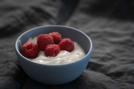 Yogurt with fresh raspberries in blue ceramic bowl on linen clothの写真素材