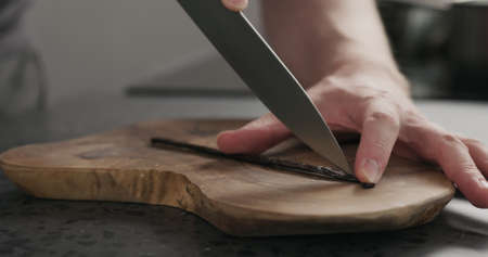 Man cut vanilla pod on olive wood boardの写真素材