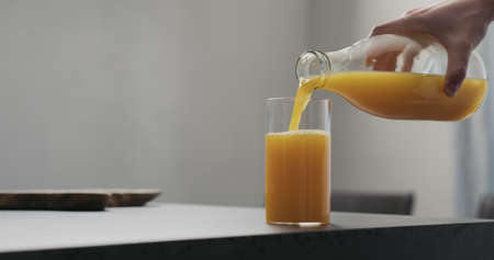 man pour orange juice from glass bottle into highball glass on concrete countertop with copy spaceの写真素材
