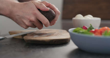 man open avocado for a salad on olive wood boardの写真素材