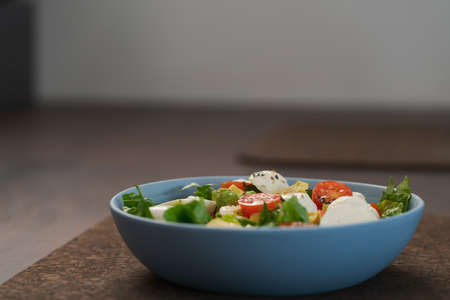 Salad with avocado, cherry tomatoes, romaine and mozzarella in blue bowl on walnut table with copy spaceの写真素材