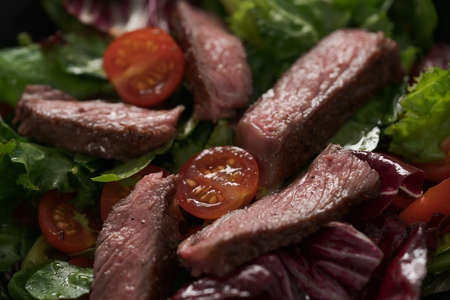 Steak salad with cherry tomatoes and mixed greens in black bowlの写真素材