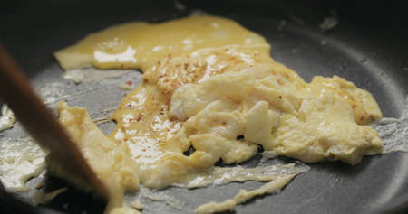 making scrambled eggs on nonstick pan, mixing with wooden spatulaの写真素材
