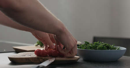 Slow motion man hands put tomatoes on top of kale in blue bowl on concrete surfaceの写真素材