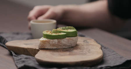 Slow motion man eating breakfast with caibatta with avocado and cream cheese and cup of espresso
