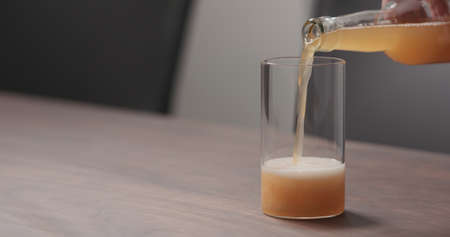 Slow motion pour orange soft drink into highball glass on walnut table with copy space