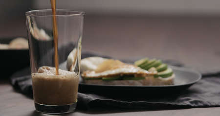 Slow motion pour stout beer into pint glass with food on background
