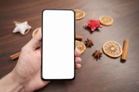 Man hand hold smarthone with white screen with christmas decorations on backgroundの写真素材