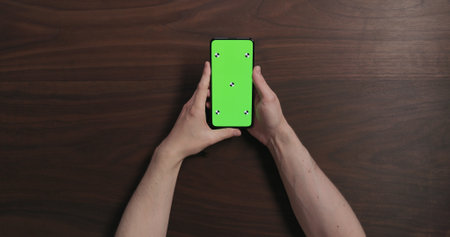 Top view man hands hold smartphone with green screen over black walnut wood tableの写真素材