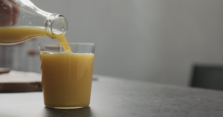 orange juice pour into thin glass from glass bottle on kitchen countertopの写真素材