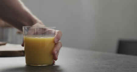 man hand take orange juice in thin glass from countertopの写真素材