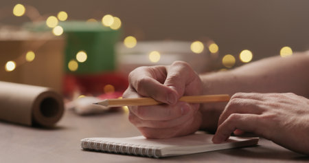 man tapping his finger thinking about christmas gifts with notepad and a pencil under warm light in the eveningの写真素材
