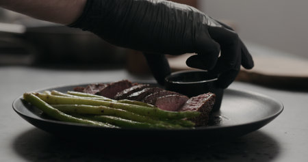man serves sliced beef steak with asparagus on black plate on concrete countertopの写真素材