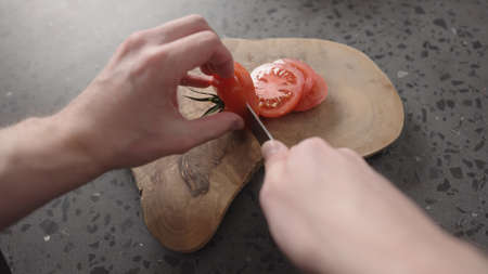 Pov shot of man slicing tomato on olive wood boardの写真素材