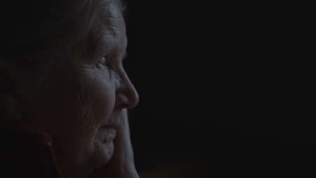 shot of old woman sitting near window dark litの写真素材