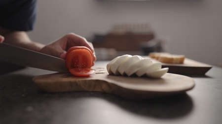 man slicing tomatoes on olive wood boardの写真素材