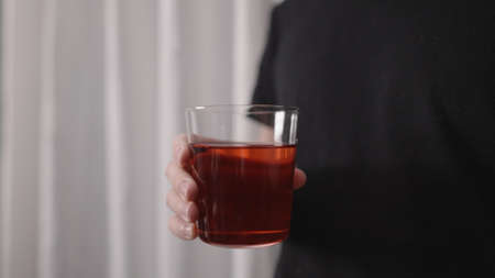 man drinking red drink from tumbler glass near window