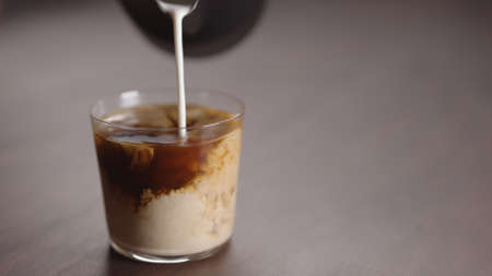 milk pour into tumbler glass with coffee on walnut tableの写真素材