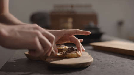 man spreading chocolate spread on baguette slices on olive board