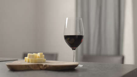 red wine into wineglass with hard cheese on background on wood tableの写真素材