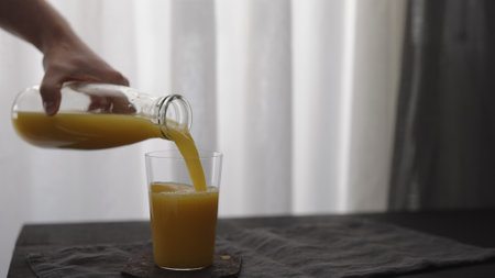 Slow motion man hand pour orange juice from glass bottle to tumbler glass on black wood tableの写真素材