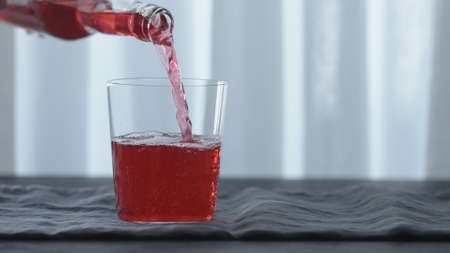 Slow motion pour pink drink in tumbler glass on black wood table with copy spaceの写真素材