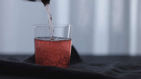 Slow motion pour pink drink in tumbler glass on black wood table with copy spaceの写真素材