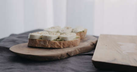 making ciabatta bruschettas with mozzarella and pesto on olive board with window on backgorundの写真素材