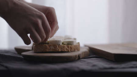 man making ciabatta bruschettas with mozzarella and pesto on olive board with window on backgorund
