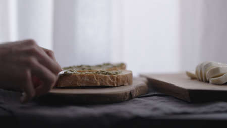 man making ciabatta bruschettas with mozzarella and pesto on olive board with window on backgorund