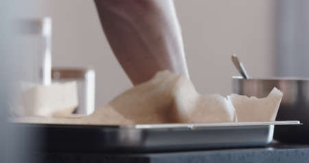 man put baking paper into tray for baking granolaの写真素材