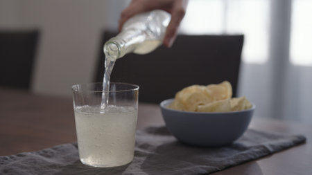 man pour ginger beer into tumbler glass with blue bowl full of potato chipsの写真素材