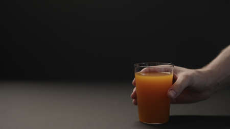 man hand take mango juice in tumbler glass on black paper background with copy spaceの写真素材