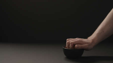 man take roasted hazelnuts from black bowl on black paper backgroundの写真素材