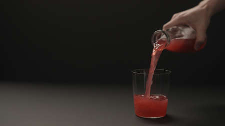 man hand pour berry drink into tumbler glass on black paper background with copy space