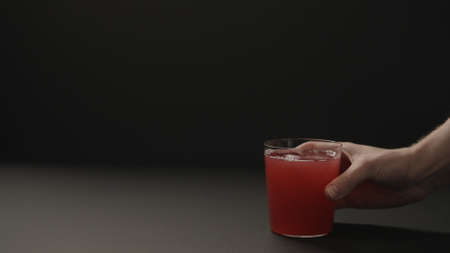 man hand take berry drink in tumbler glass on black paper background with copy space