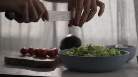 man cutting cherry tomatoes into salad with window backlight