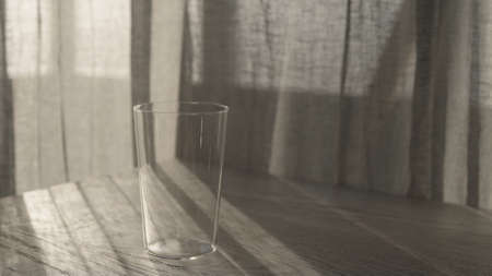 thin tumbler glass on white oak table with curtains sways on the wind on background with sunset...